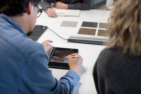 AHR colleague using stylus on tablet during a collaborative design reviews, with others reviewing material samples on table nearby.