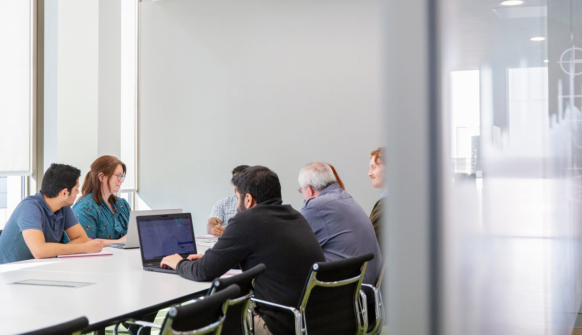 AHR building consultancy meeting in a collaborative workspace in an AHR office, with people in discussion and someone working on a laptop..