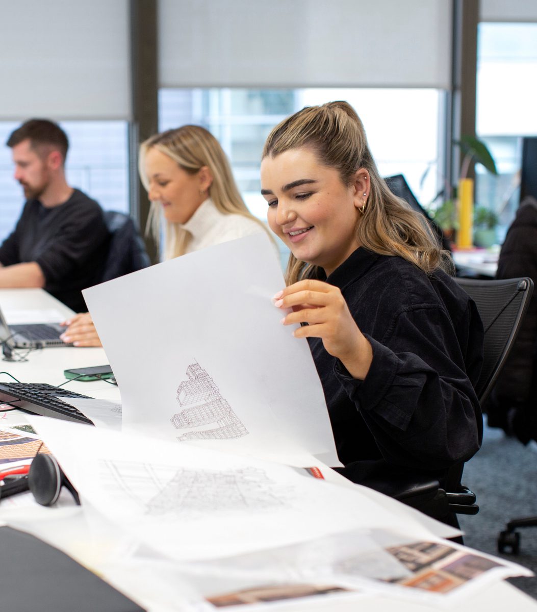Three AHR colleagues sat on a row of desks with drawings and sketches in the foreground.