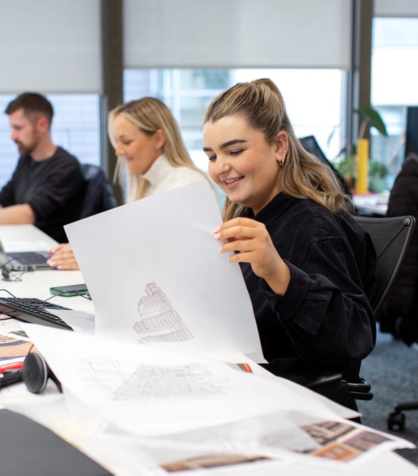 Three AHR colleagues sat on a row of desks with drawings and sketches in the foreground.