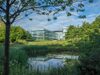 The whole office building and its vast nature surroundings with a pond and trees in the foreground.
