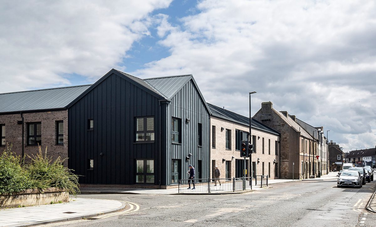 The exterior of the Passivhaus residential development at 1- 21 St Cuthberts, with redbrick, black cladding and including the surrounding area.