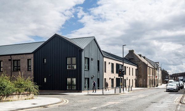 The exterior of the Passivhaus residential development at 1- 21 St Cuthberts, with redbrick, black cladding and including the surrounding area.
