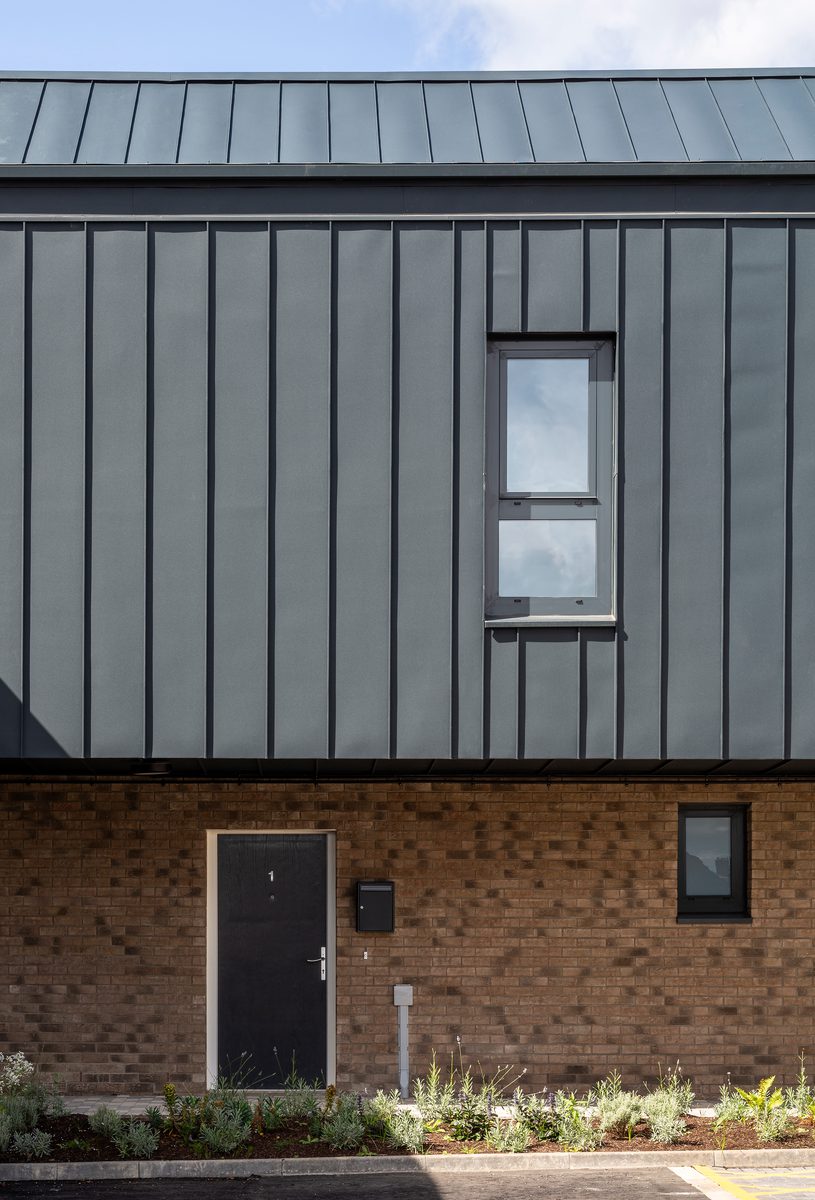 A portrait shot of the black cladding on the residential building with planting below.