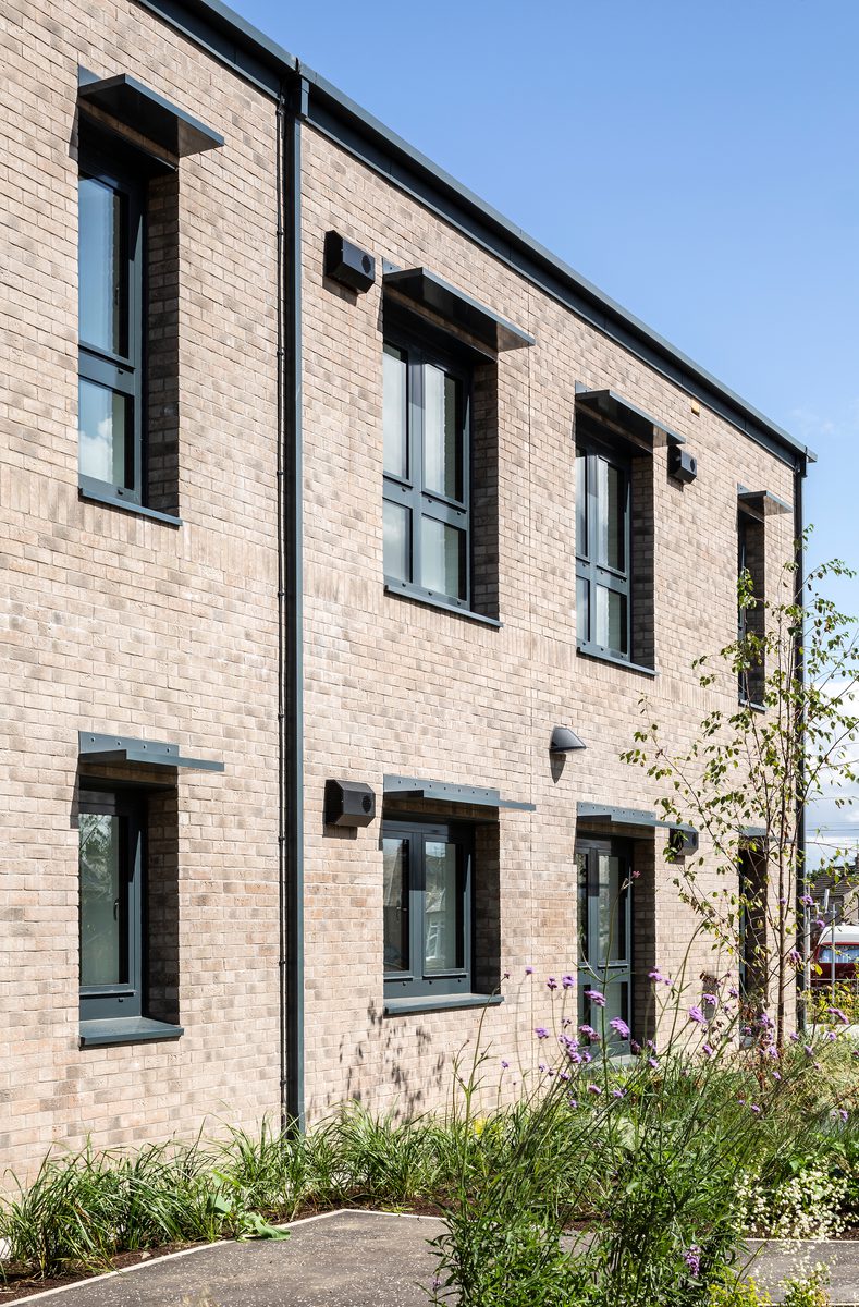 A portrait shot of the exterior showing the brickwork and planting in the foreground.