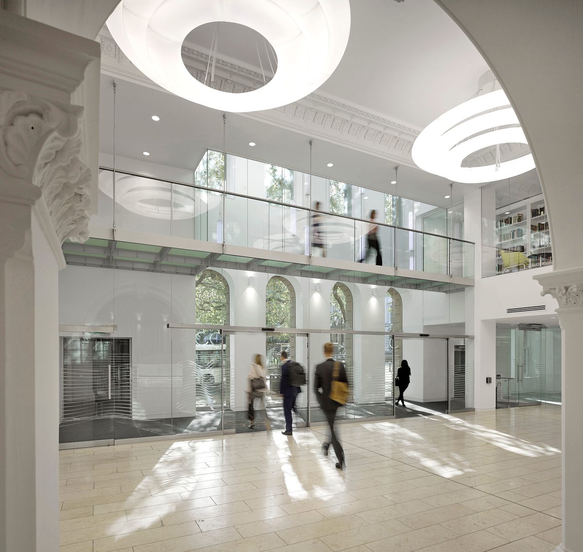 People moving around the bright interior entrance of 55 Colmore Row, with heritage features, first floor glass bridge and bespoke lighting above.