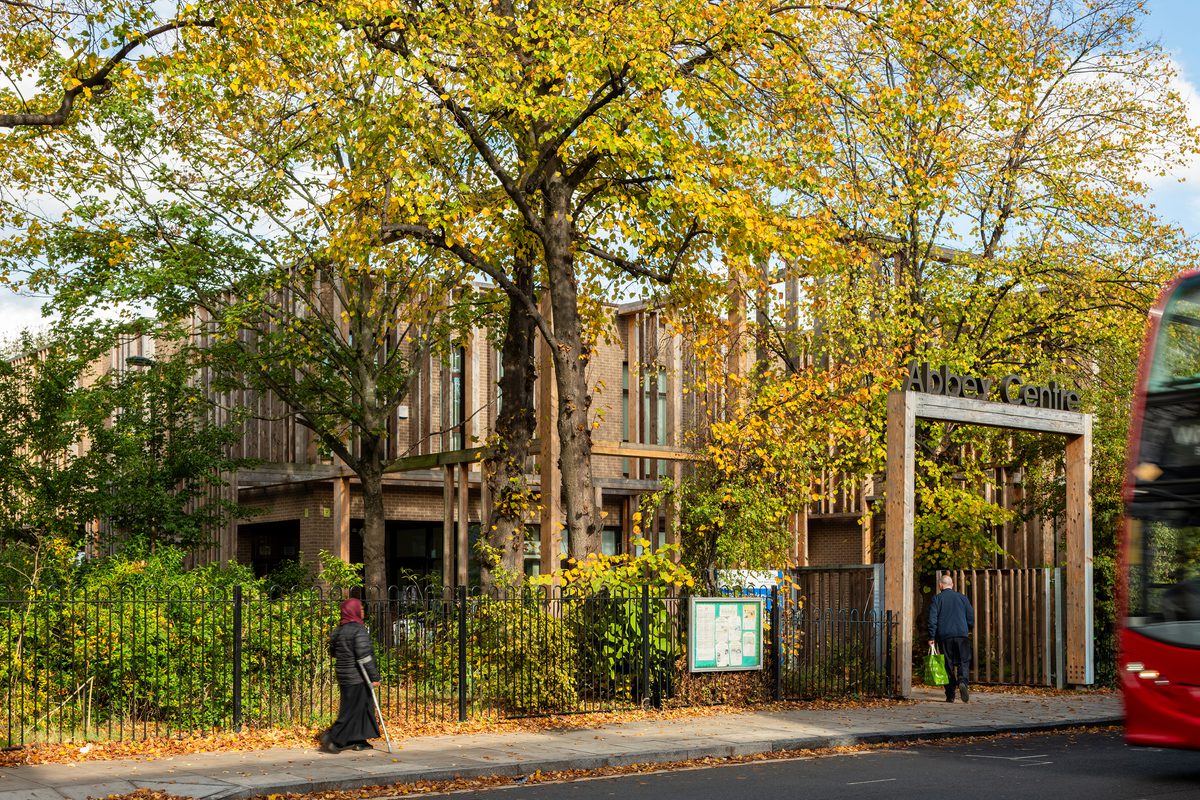 The main entrance to Abbey Area Community Hub in Camden with lots of trees and greenery in the foreground and people entering the building.