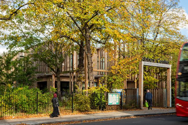 The main entrance to Abbey Area Community Hub in Camden with lots of trees and greenery in the foreground and people entering the building.