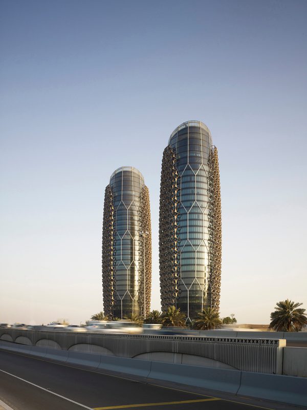 The distinctive dynamic facade shines as the two towers of the Al Bahr Towers stand alone against a clear sky.
