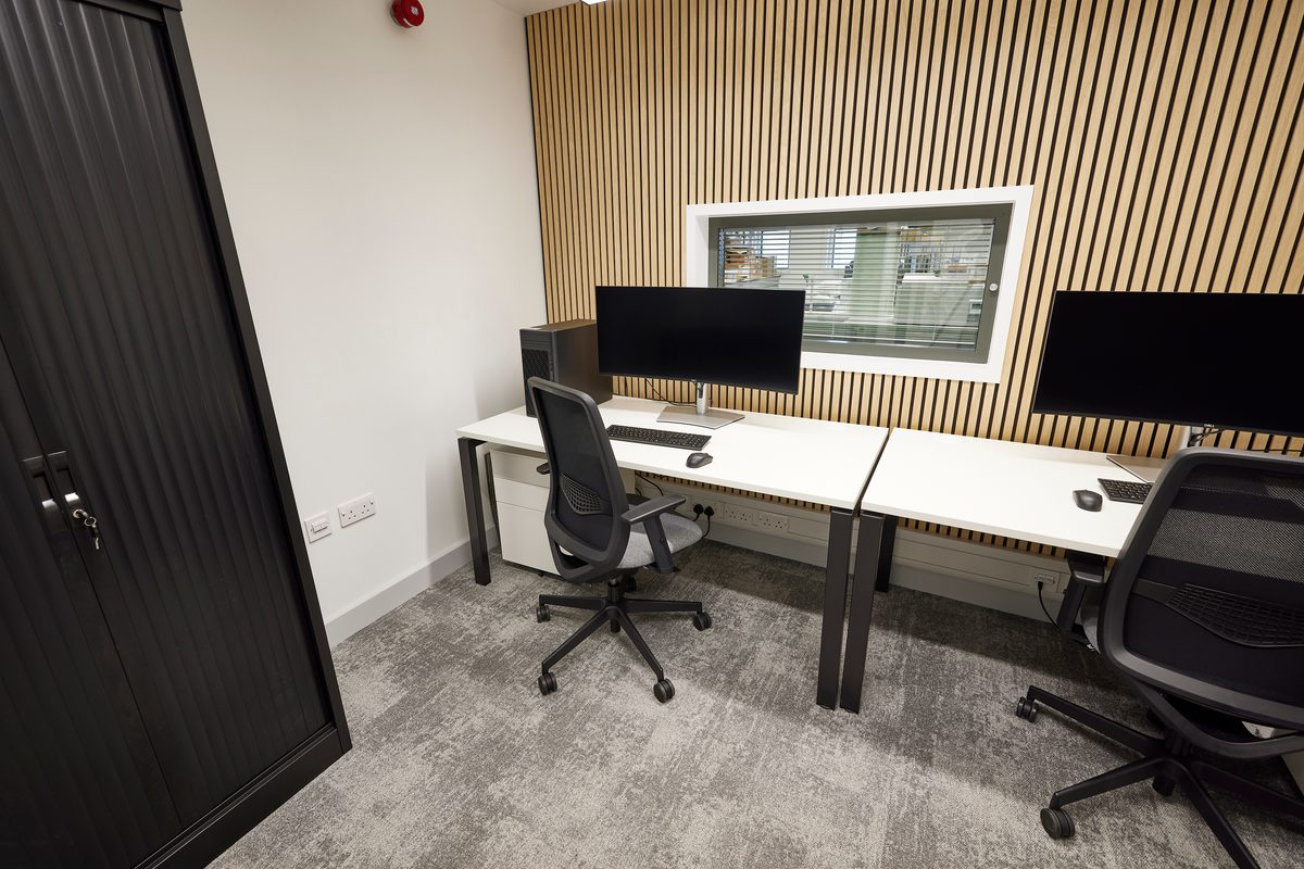 A separate workspace area with two desks, chairs and monitors and wooden panelling in the background.