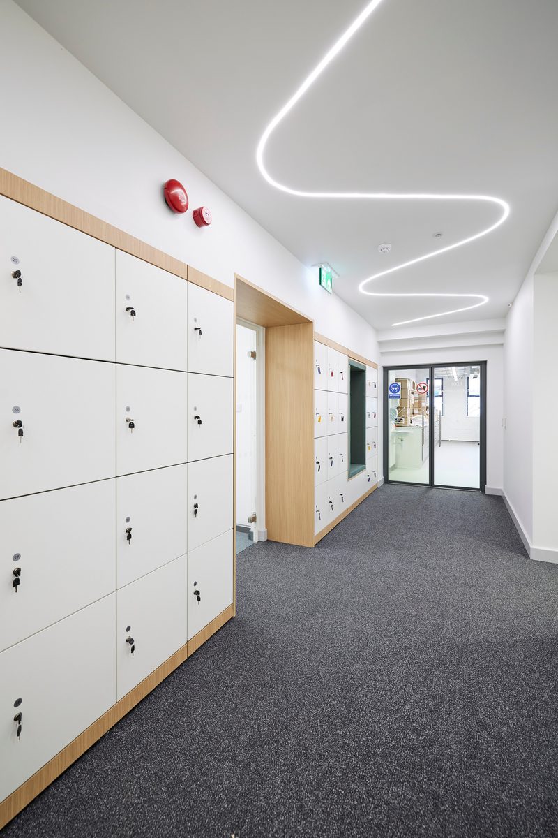 The brightly lit corridor with lockers down the side and a creative light feature running down the ceiling.