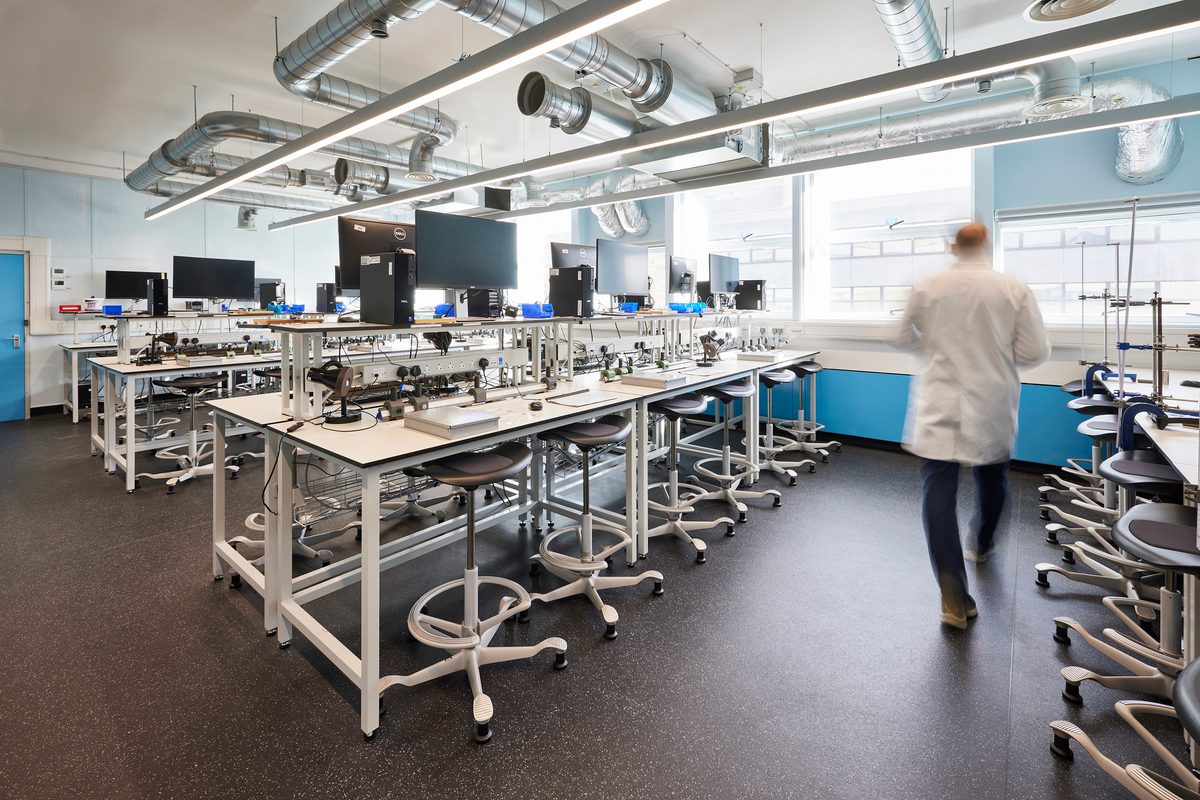 A man walking across the room filled with workspace and computers in a lab coat.