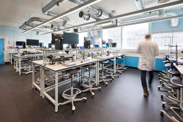 A man walking across the room filled with workspace and computers in a lab coat.