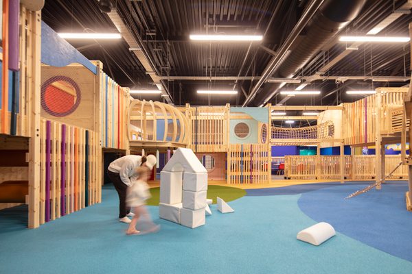 The wooden play frames with an adult and child in the foreground playing in the colourful space.