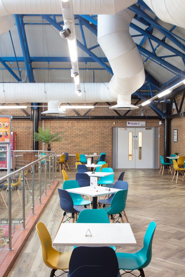 Brightly coloured seating and tables on the mezzanine level within the refurbished Barnsley Metrodome reception, with glazed balustrade and exposed brickwork.