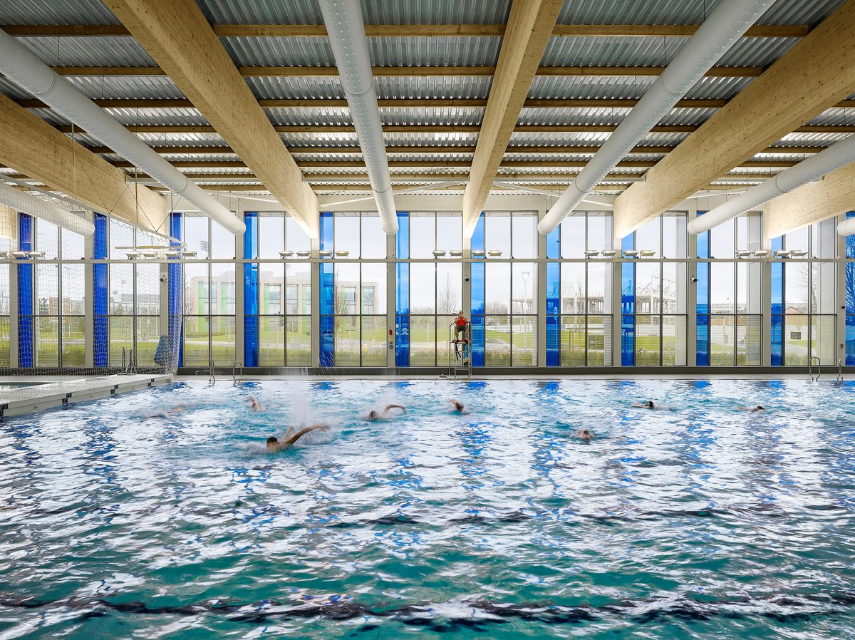 People swimming within the bright leisure centre pool within Beswick Community Hub masterplan, with highly glazed façade.
