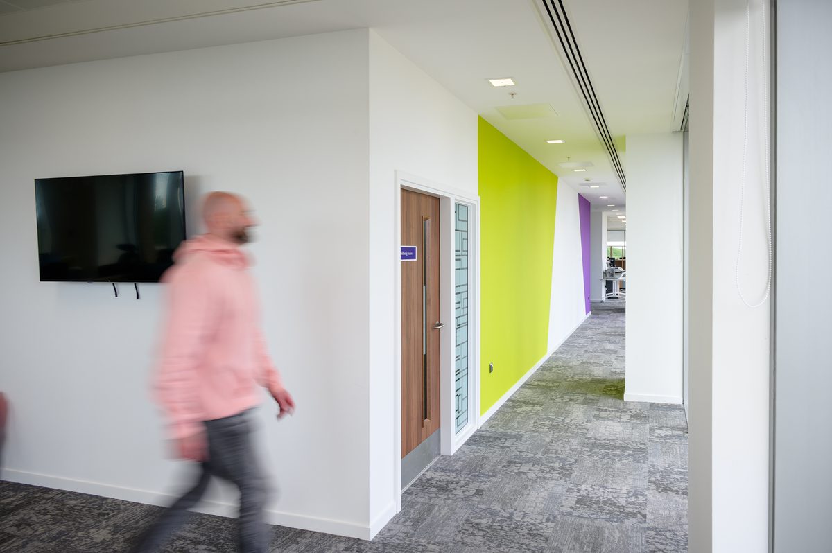 Somebody walking through the the Children and Family Court Advisory and Support Service office, with bright white walls and a lime green feature wall.