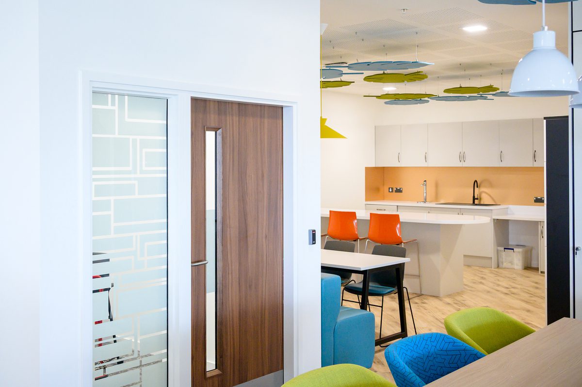 The bright, communal kitchen area within the Children and Family Court Advisory and Support Service office, with colourful furniture and fixtures.