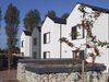 The bright white exterior of some terraced houses within the Cameron Close development, with cabled rooves and trees surrounding.