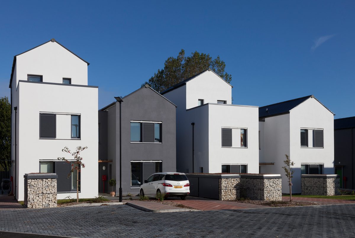 An exterior face of the Cameron Close residential development with bright white and grey facades, parking facilities and access routes in front.