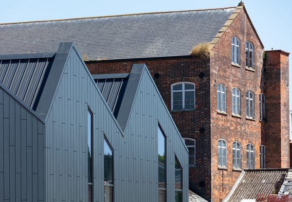 A exterior detail shot of slate grey metal cladding , saw tooth roof and a mill adjacent to Chard Leisure Centre..