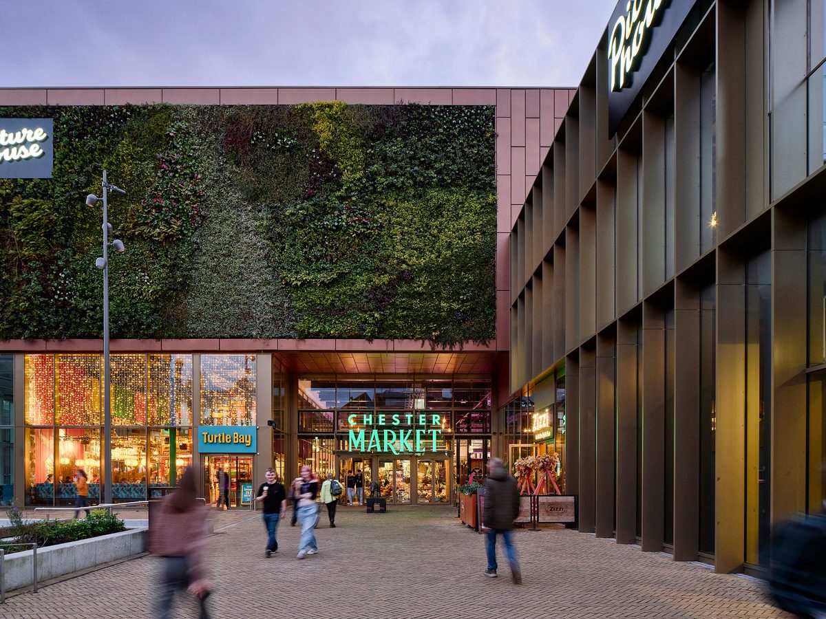 People enjoying the communal public square within the Chester Northgate development, at dusk with the planted green wall of the market hall in the background.