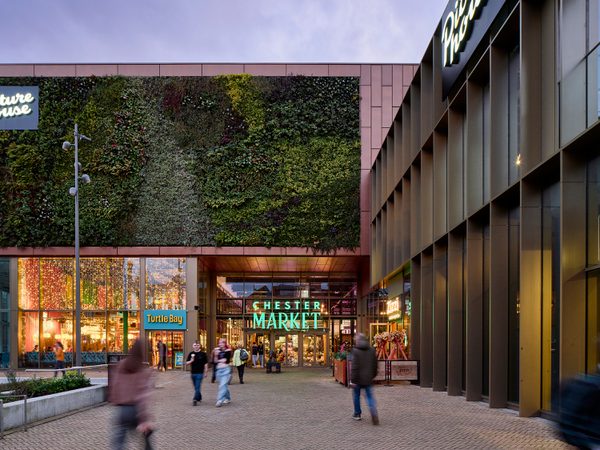 People enjoying the communal public square within the Chester Northgate development, at dusk with the planted green wall of the market hall in the background.