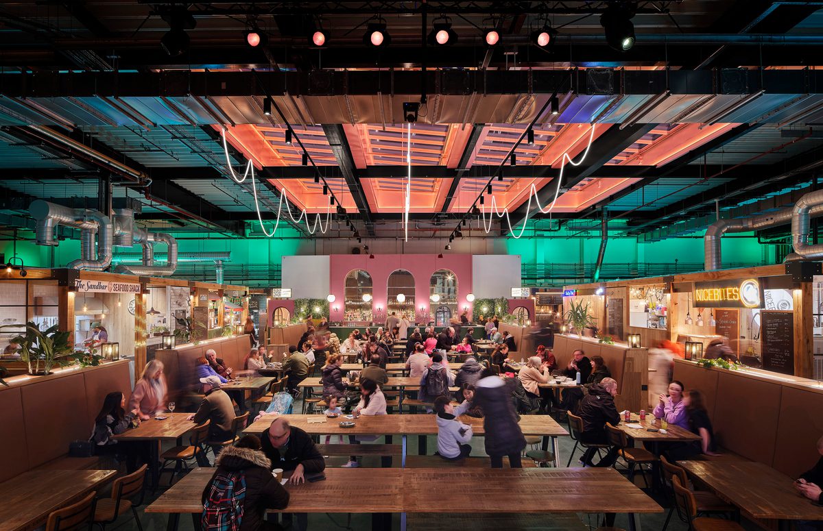 The bright, colourful interior of the refurbished, listed market hall with diners eating in a central space with food and beverage offerings surrounding.