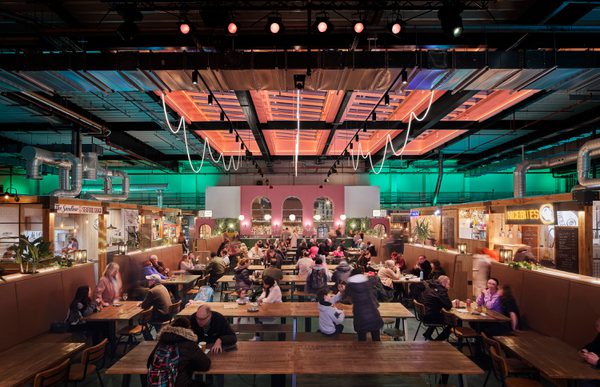 The bright, colourful interior of the refurbished, listed market hall with diners eating in a central space with food and beverage offerings surrounding.