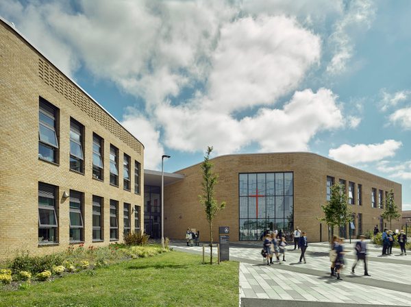 An exterior shot of the entrance to Christ the Word Catholic School, with extensive landscaping and planting and students walking in front of the building.
