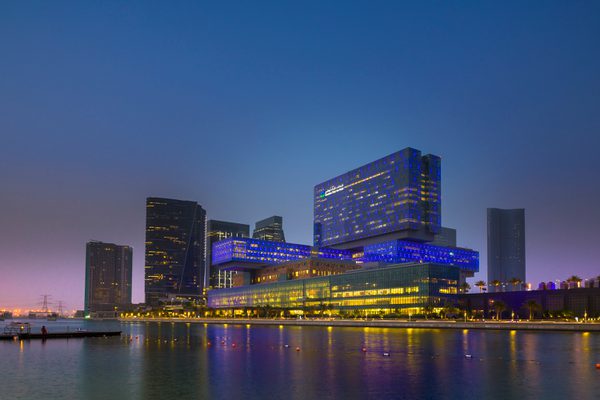 The exterior of the completed Cleveland Clinic hospital at night with blue lighting and ample windows allowing for plentiful natural lighting, on the Al Maryah waterfront.