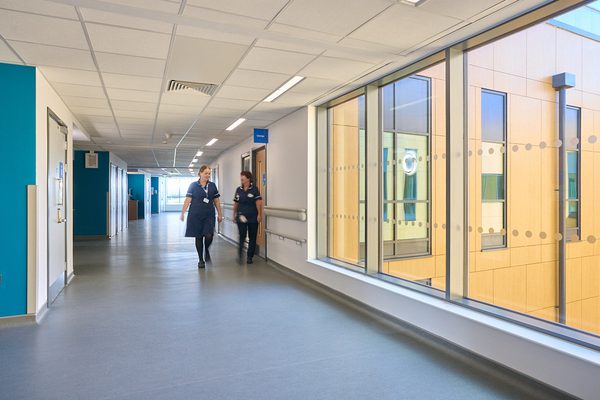 Two staff members walking down a bright corridor next to a window with plenty of daylight.