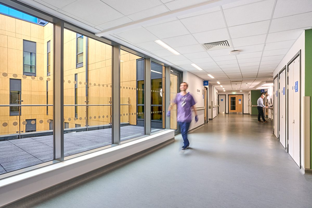 A staff member walking down a bright and daylight-filled corridor with views of the terrace outside.