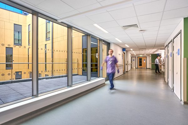 A staff member walking down a bright and daylight-filled corridor with views of the terrace outside.