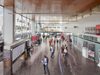 A busy, spacious concourse inside Coventry Station with high wood-paneled ceilings, large glass windows, and people moving through the hall.