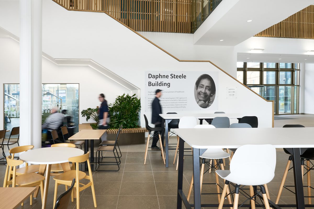 An interior of the cafe area inside the building, with the Daphne Steele mural in front and people interacting in the sociable space.