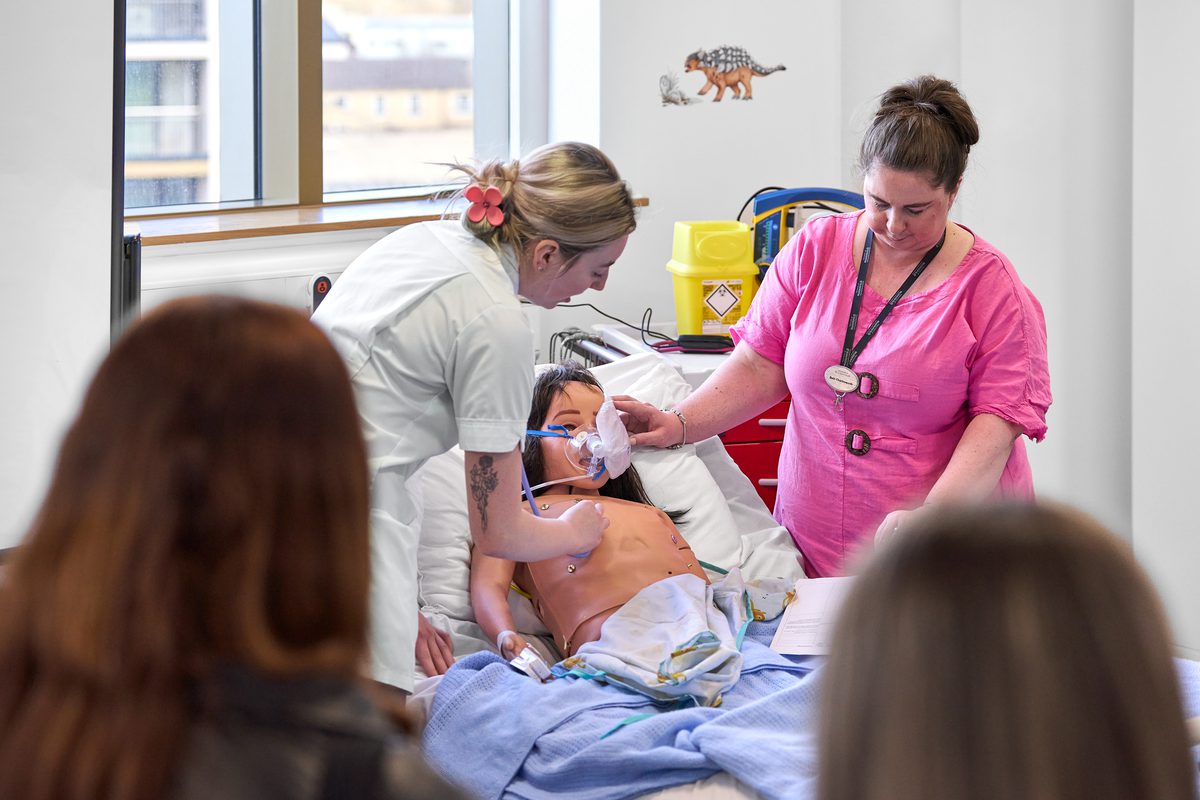 Members of staff simulating a healthcare scenario inside the building with a group of people overlooking for learning.
