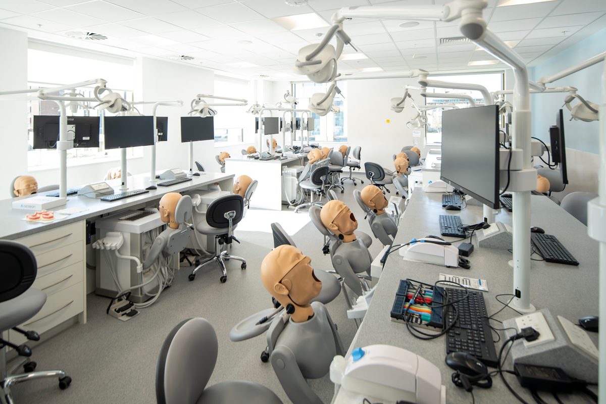 A row of dental phantom head simulators in the Emily Siddon Building, mounted on chairs and workbenches that mimic a real dental operatory. On the desks is computer equipment for students.