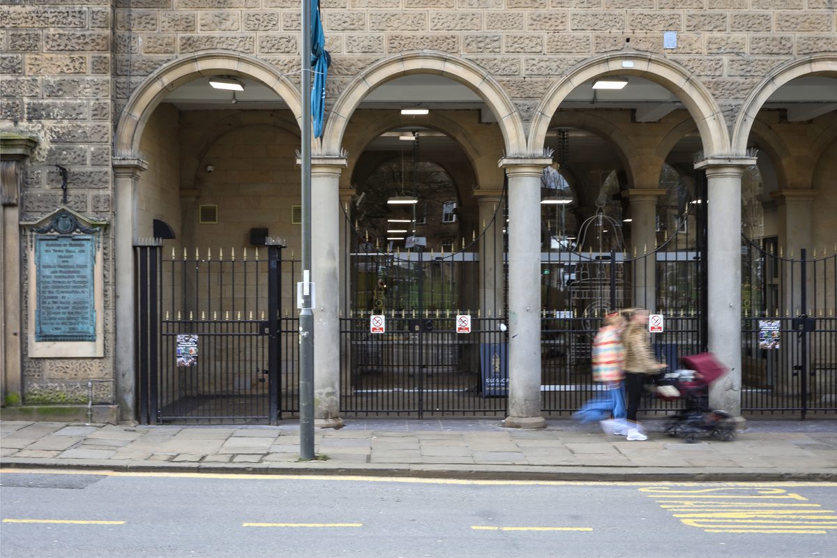 The external view into the town and market hall behind a bus stop with a family moving across the path in the foreground.