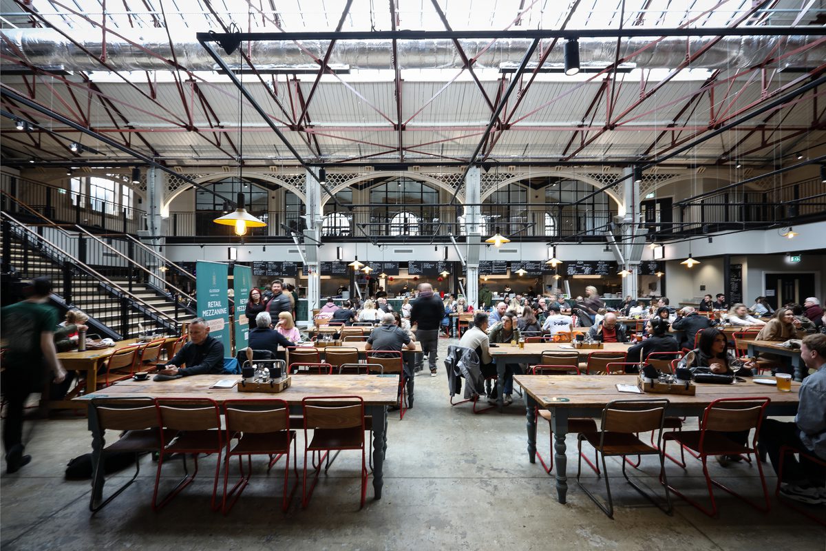 A wide shot of the indoor market food hall full with families enjoying time together across a series of tables and benches.