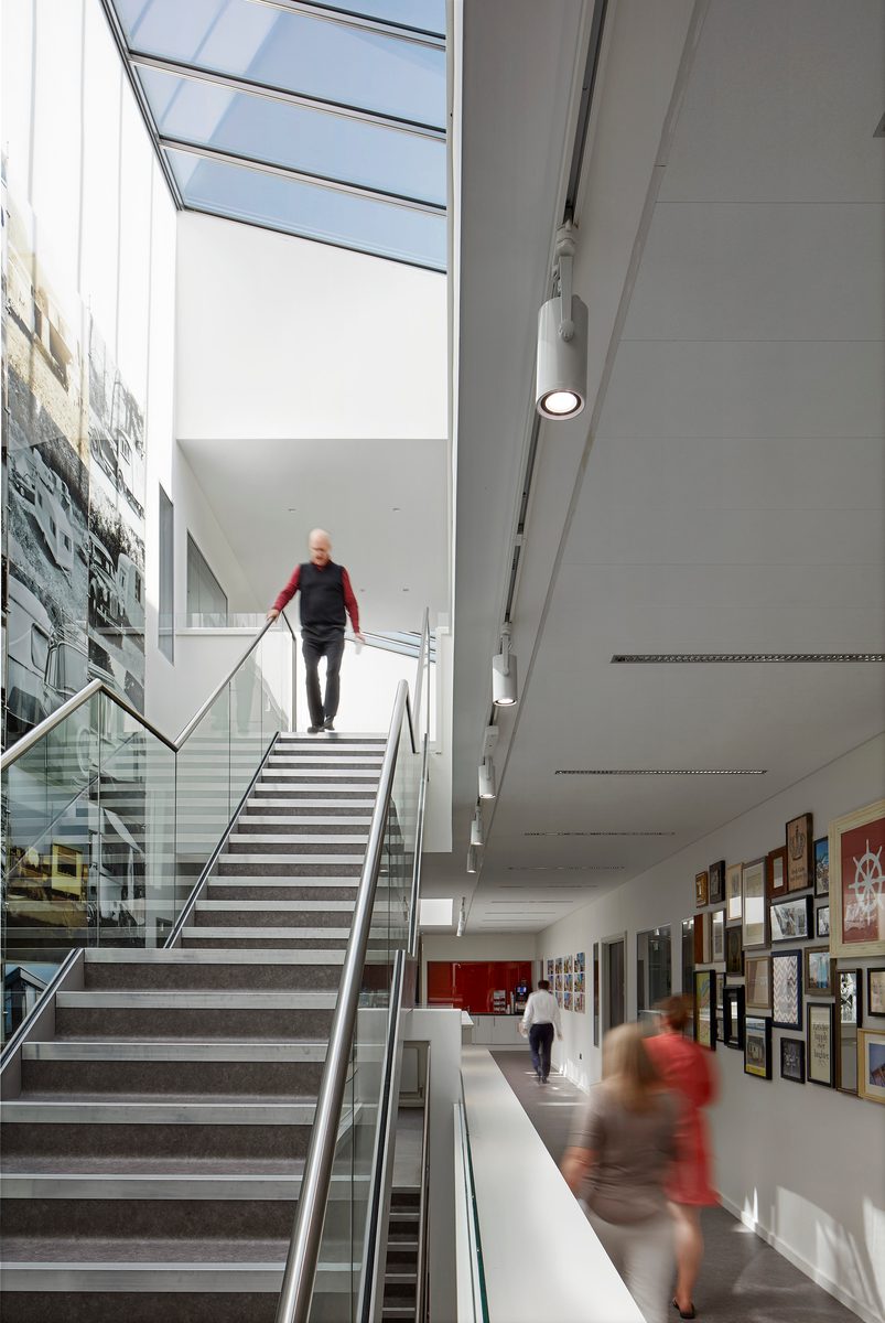 People walking through the large double height bright central atrium of Glovers House, with roof lights overhead.