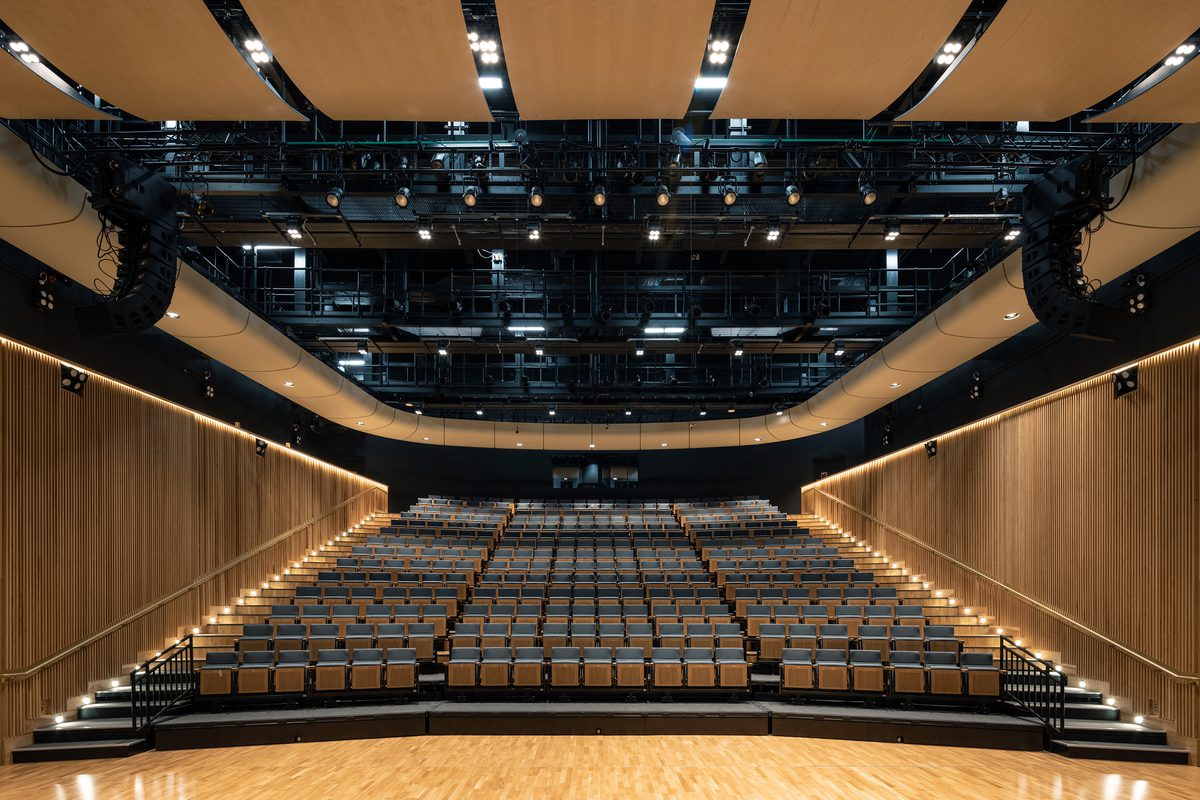 Performance hall viewed from the stage area surrounded by retractable seating, timber detailing and exposed services.