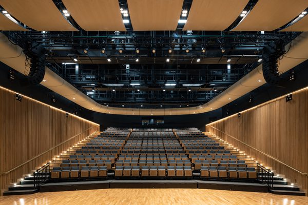 Performance hall viewed from the stage area surrounded by retractable seating, timber detailing and exposed services.