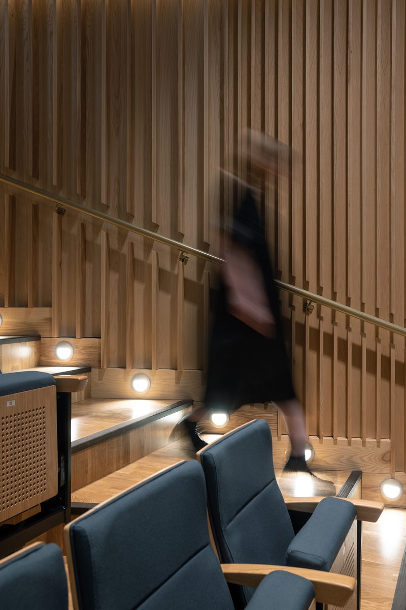 A detail image showing timber detailing at the East Quad Building's performance hall, with a woman walking down the stairs.