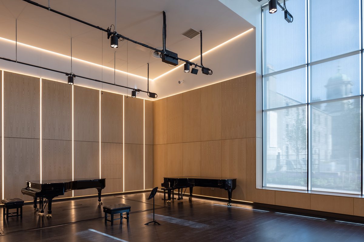 East Quad Building practice room with gold detailing, overhead lighting and a grandstand pianos, maintaining views to the wider campus.