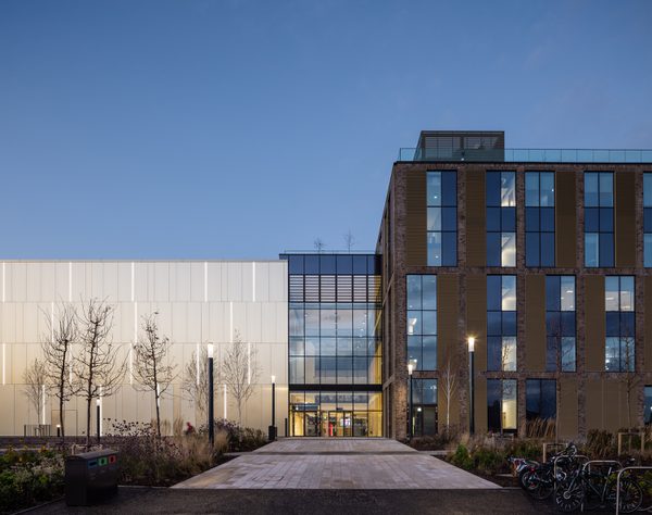 The striking exterior entrance to the East Quad building at dusk, with extensive glazing across the facade.