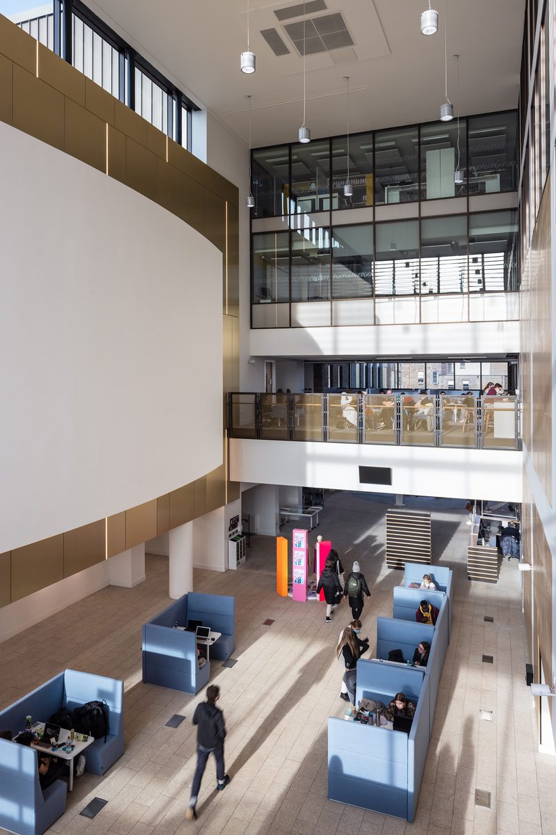 Double height atrium space of East Quad Building showing, natural light, furnishings and students moving through the space.