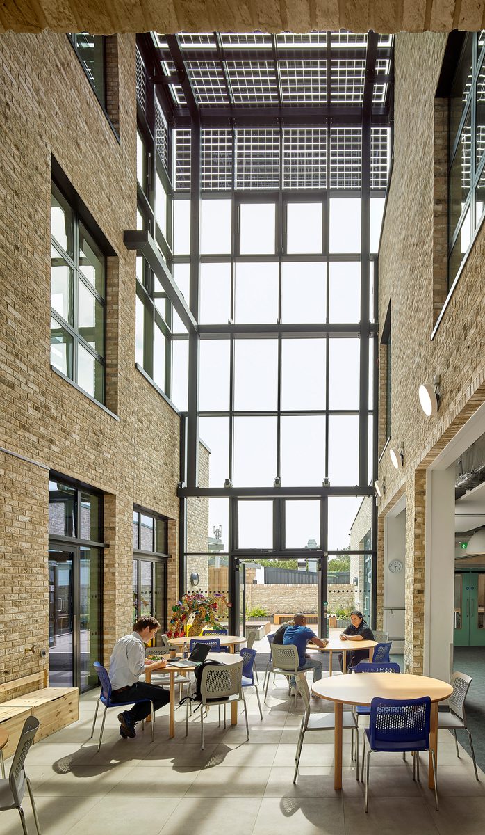A long interior shot of the greenwood centre's communal area with floor to ceiling windows and people sat in comfortable seating areas.