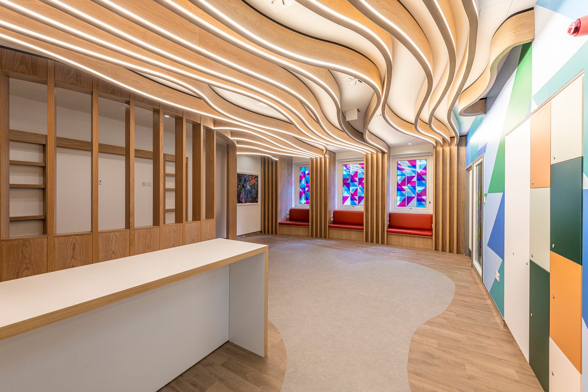 The bright, airy reception interior of the Guy's and St Thomas' Cancer ward, with white oak finishes and coloured wall graphics.