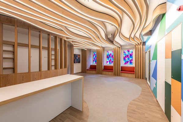 The bright, airy reception interior of the Guy's and St Thomas' Cancer ward, with white oak finishes and coloured wall graphics.